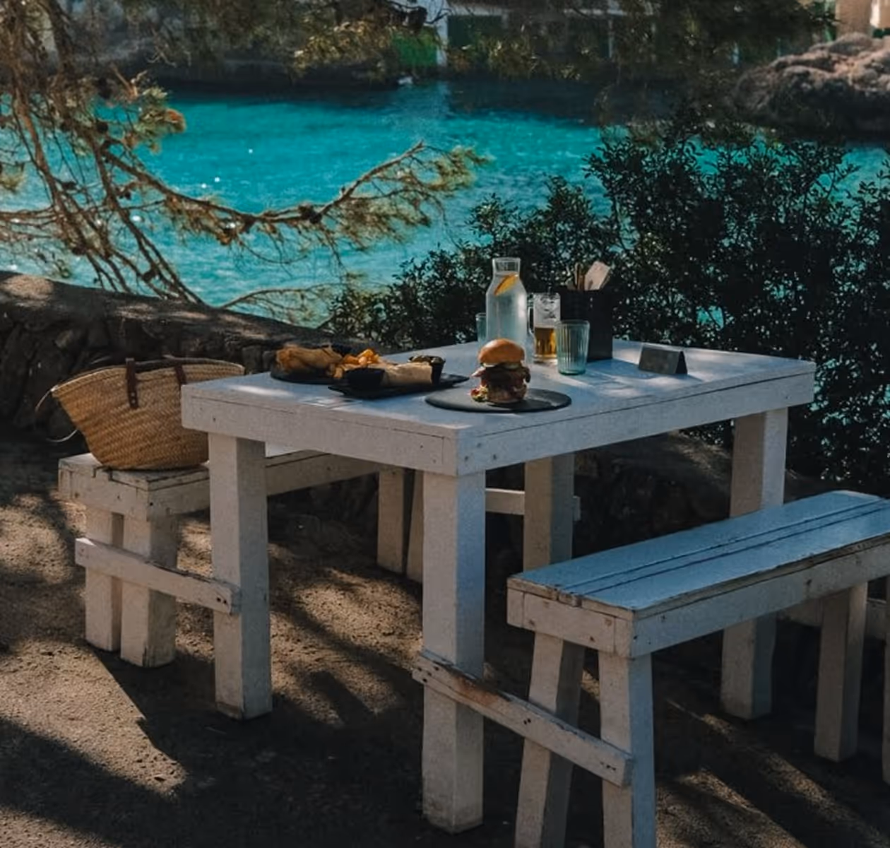 Rustic white table set with food on a terrace above a turquoise cove