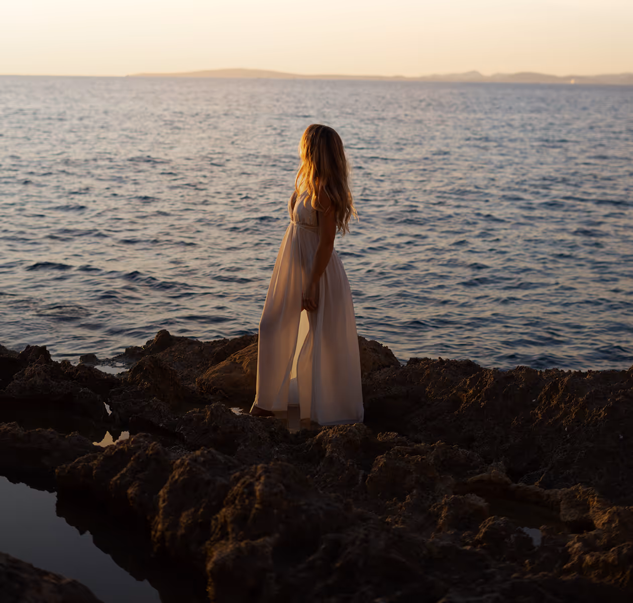 Julia in a flowing dress on coastal rocks at golden-hour sunset