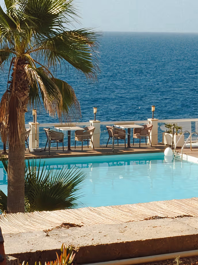 Poolside terrace with dining tables and a palm overlooking the sea