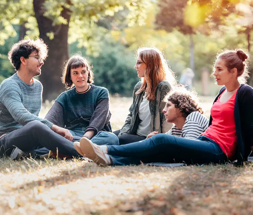Gruppe von Studierenden sitzt im Park auf dem Gras und unterhält sich entspannt.