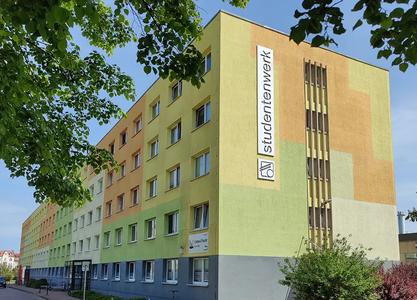 Das Wohnheim vor der Neugestaltung mit gelb-, orange- und grünfarbenen Muster und einem vertikalen Schild mit der Aufschrift 'studentenwerk' an der Fassade.
