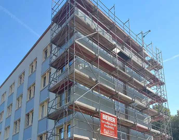 Mehrstöckiges Gebäude mit Gerüst an der Fassade und klarem Himmel im Hintergrund.