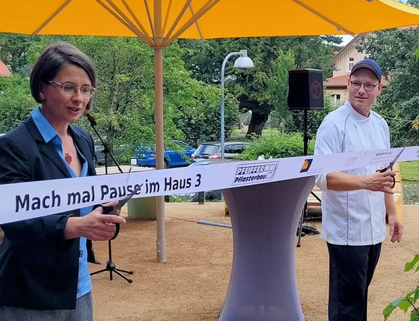 Zwei Personen schneiden mit Scheren ein Band mit der Aufschrift 'Mach mal Pause im Haus 3' durch.