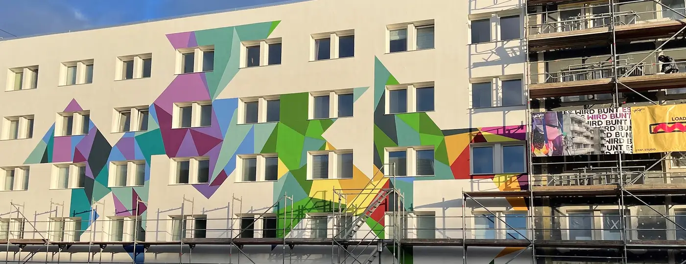 Die Fassade des mehrstöckigen Wohnheims während der Neugestaltung mit farbigen geometrischen Mustern und Gerüst davor.