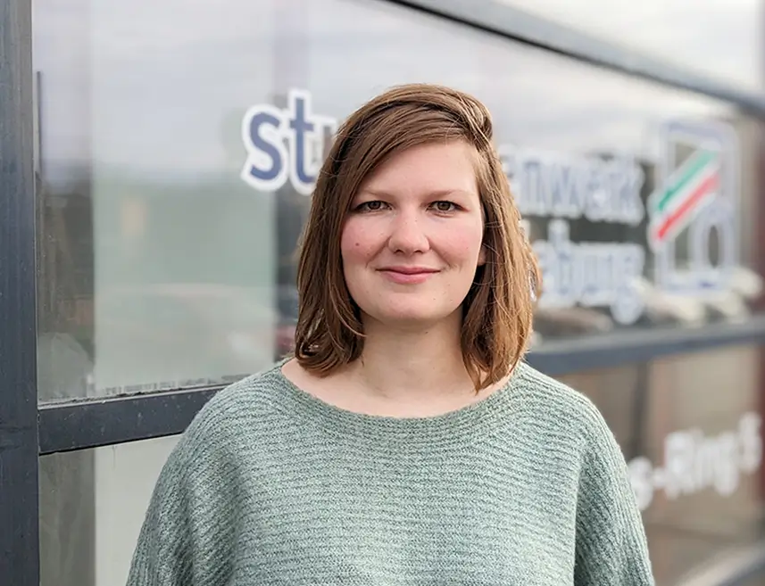 Franziska Kaiser steht vor einer Glasfassade mit teilweise sichtbaren Logo des Studentenwerk Magdeburg.