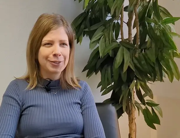 Jennifer Beder sitzt auf einem Stuhl vor einer großen Zimmerpflanze und spricht.