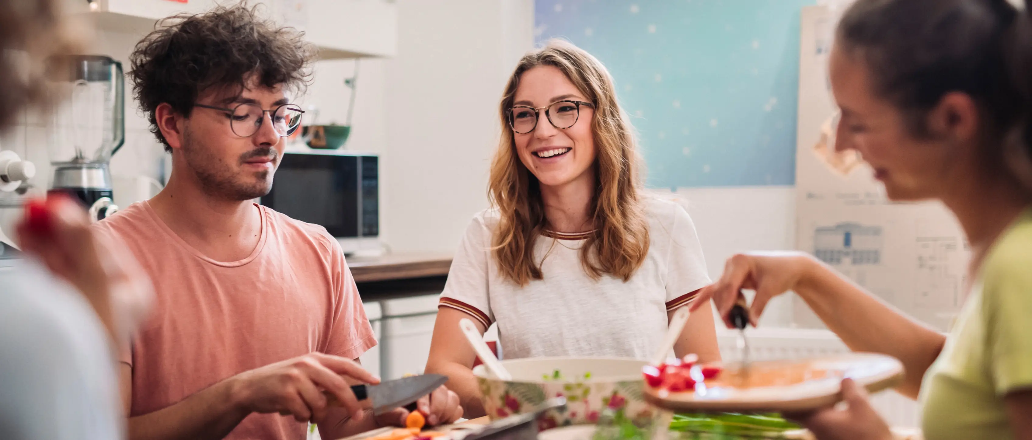 Vier junge Personen sitzen an einem Tisch in einer Wohnküche und essen gemeinsam.
