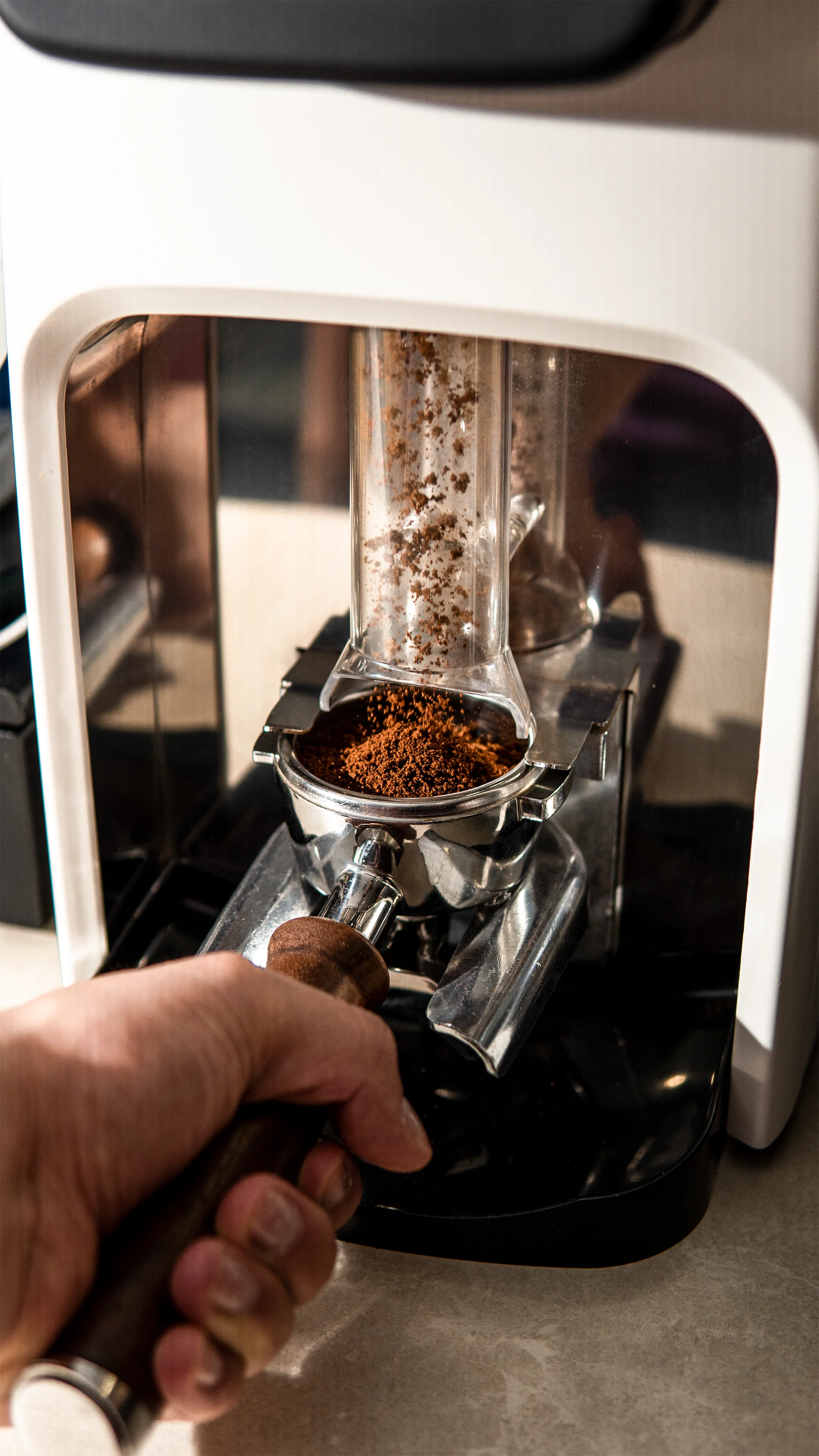 Hand holding a portafilter under a grinder dispensing fresh ground coffee.
