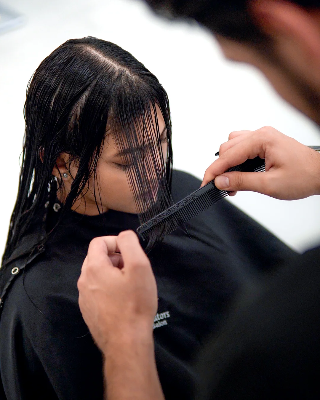 Hairdresser combing and preparing to cut a woman's wet hair in a salon.