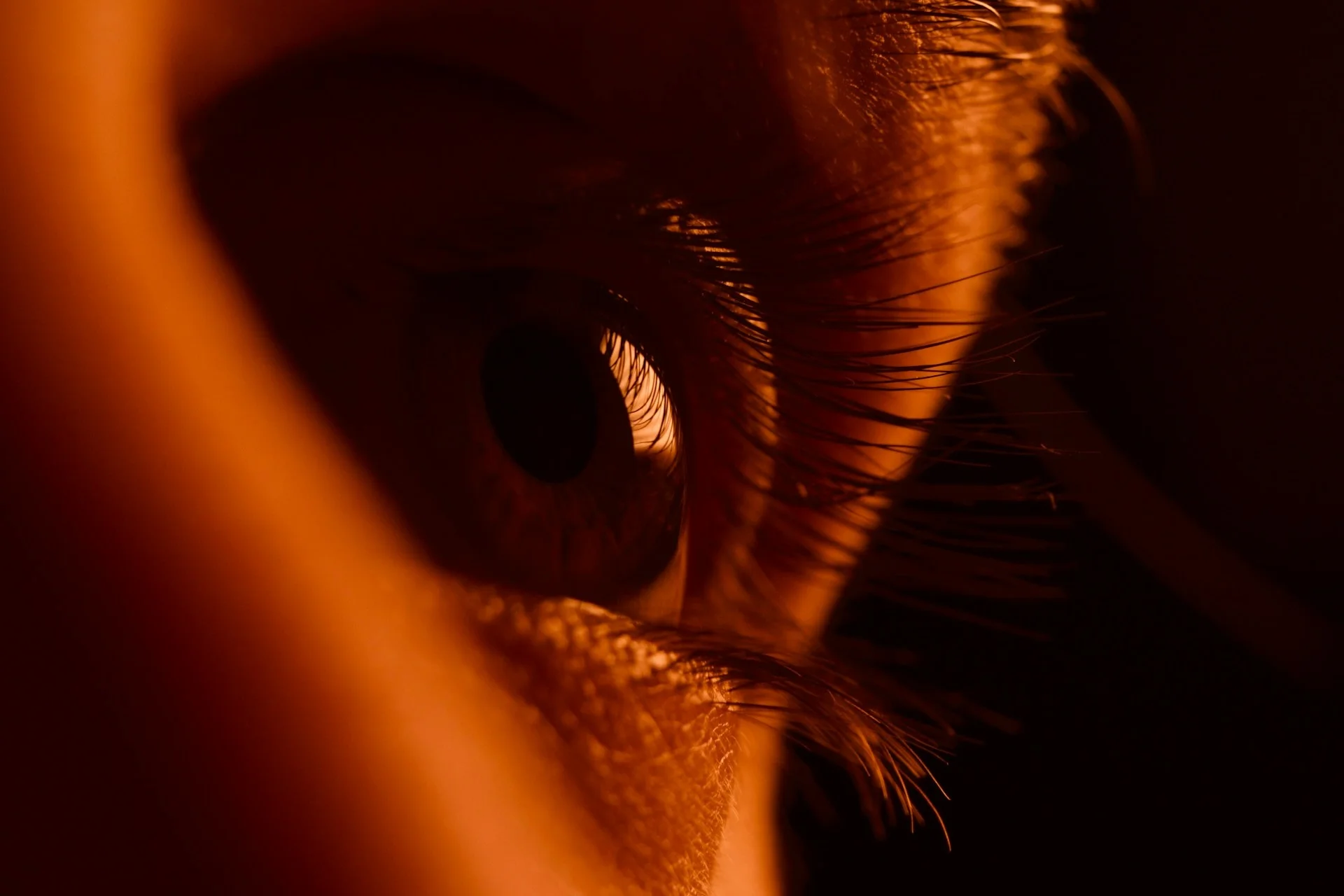 Close-up of a human eye with detailed eyelashes illuminated by warm orange lighting.