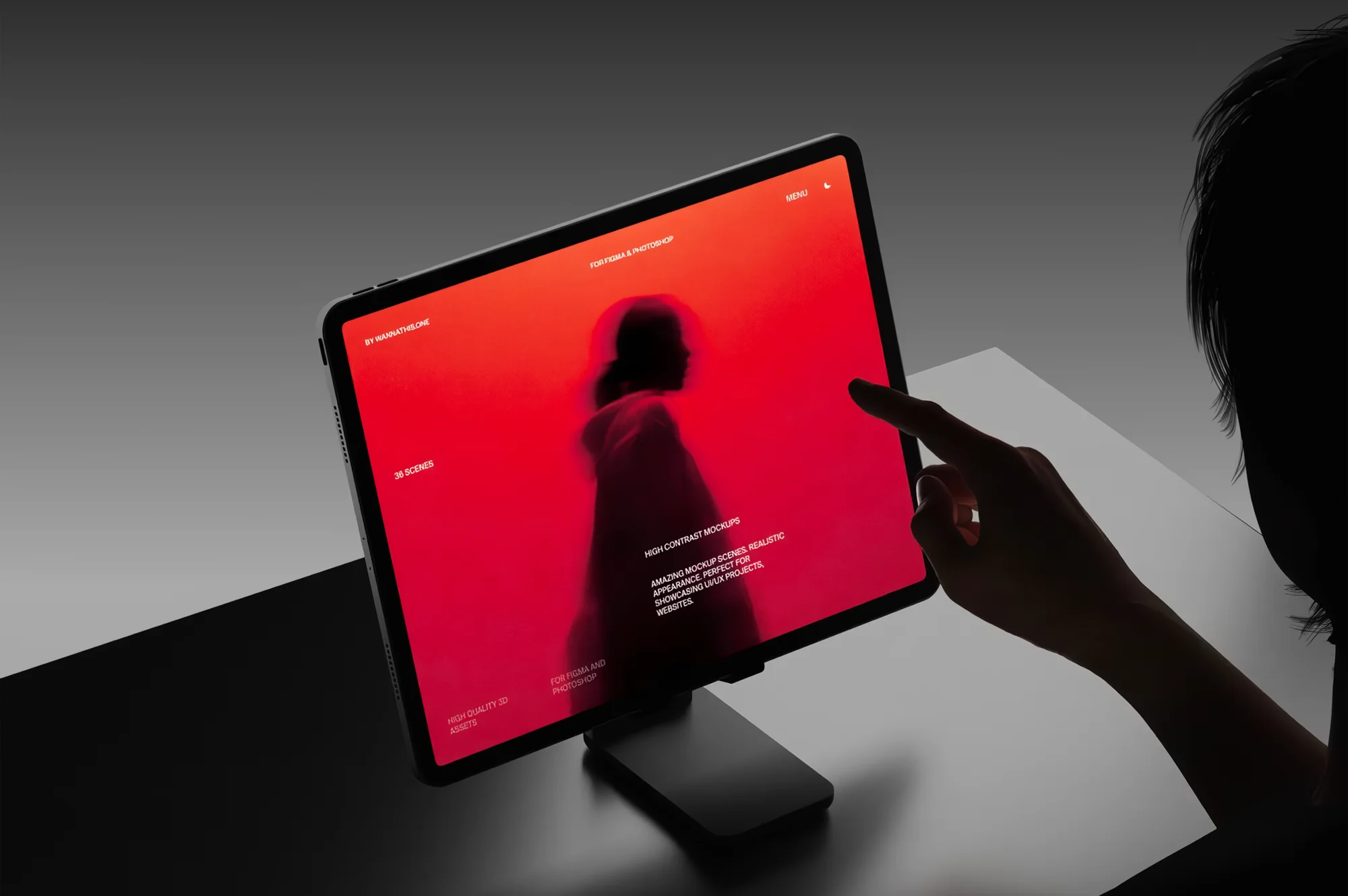Silhouetted hand reaching toward a tablet on a stand displaying a red screen with a blurred profile of a person in a hoodie.