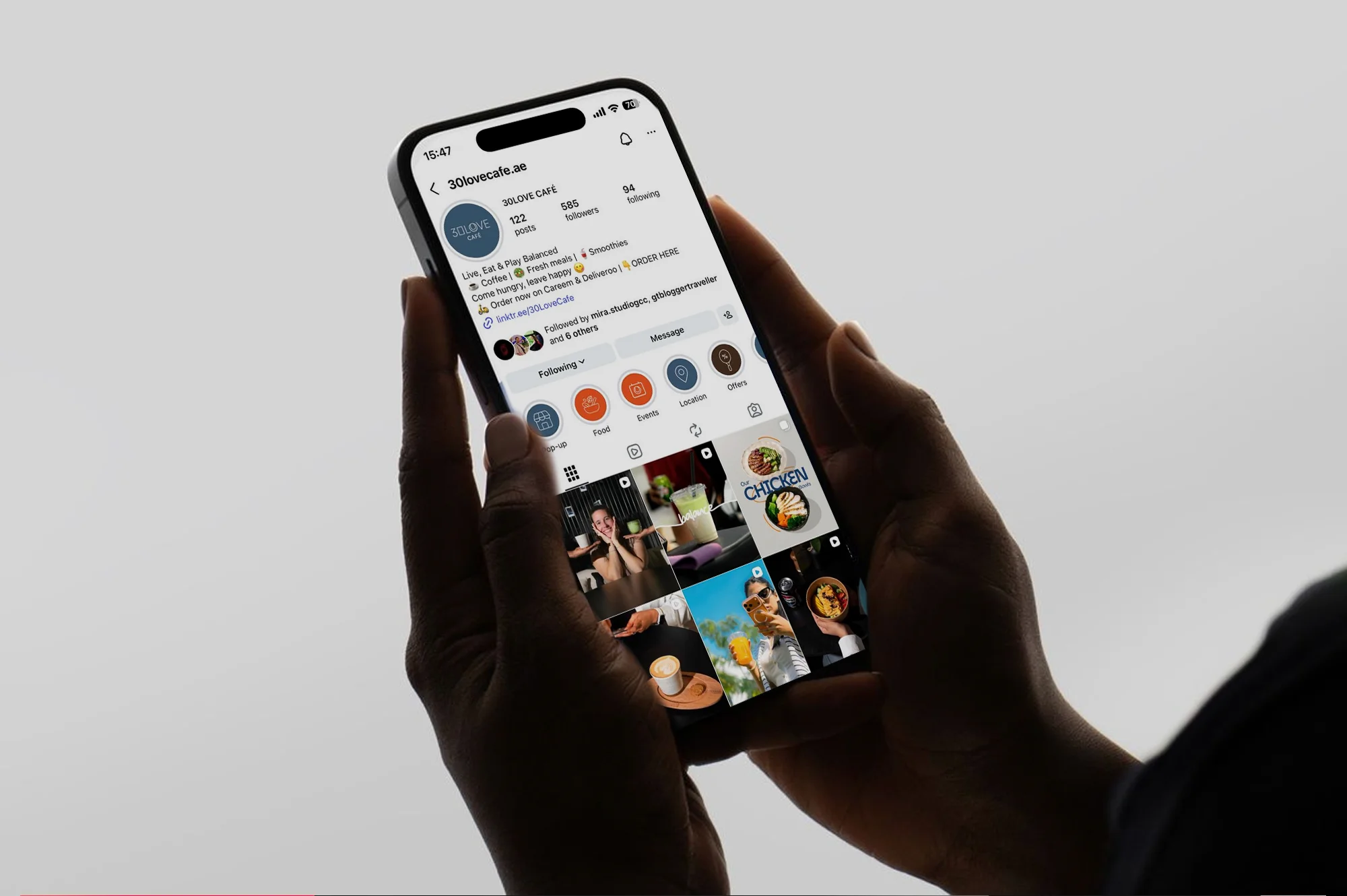 Person holding a smartphone showing the Instagram profile of 30lovecafe.ae featuring posts of food and drinks.