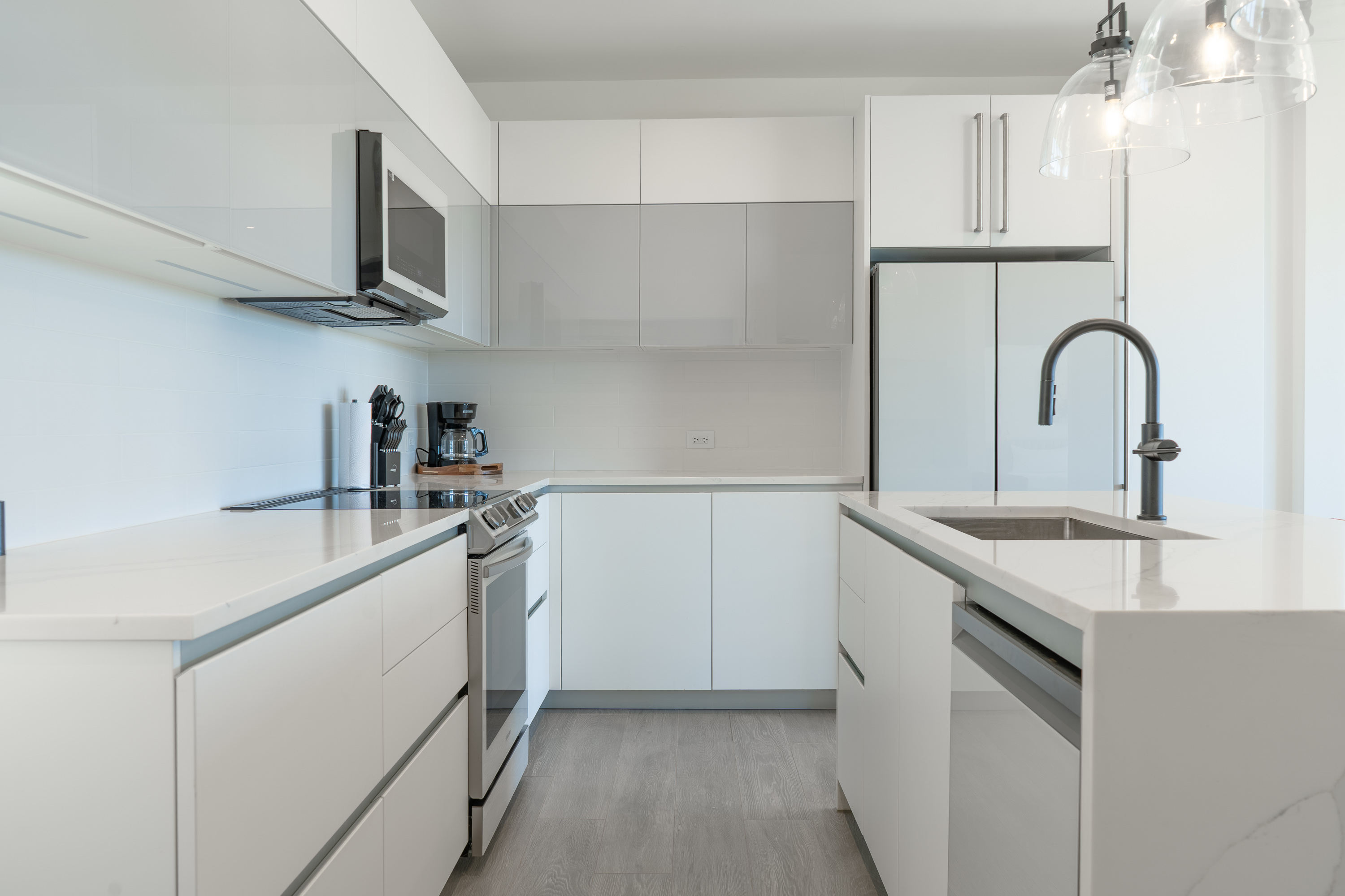Modern white kitchen with stainless steel stove, microwave, refrigerator, and island with sink and black faucet.