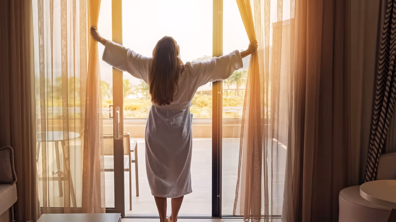 Woman opening curtains in hotel room