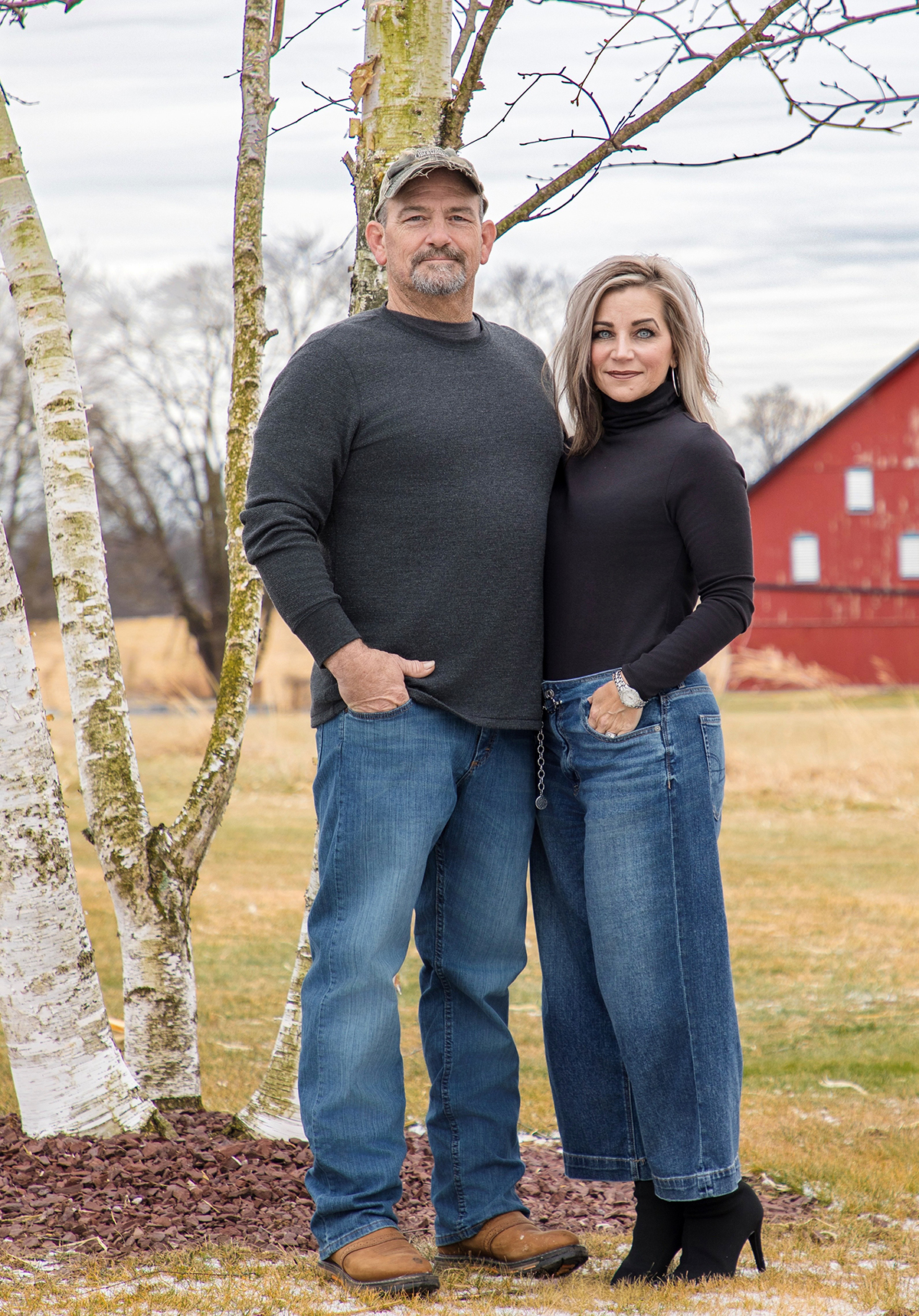 Catherine Wallen and her husband standing together outdoors in front of birch trees and a red barn.