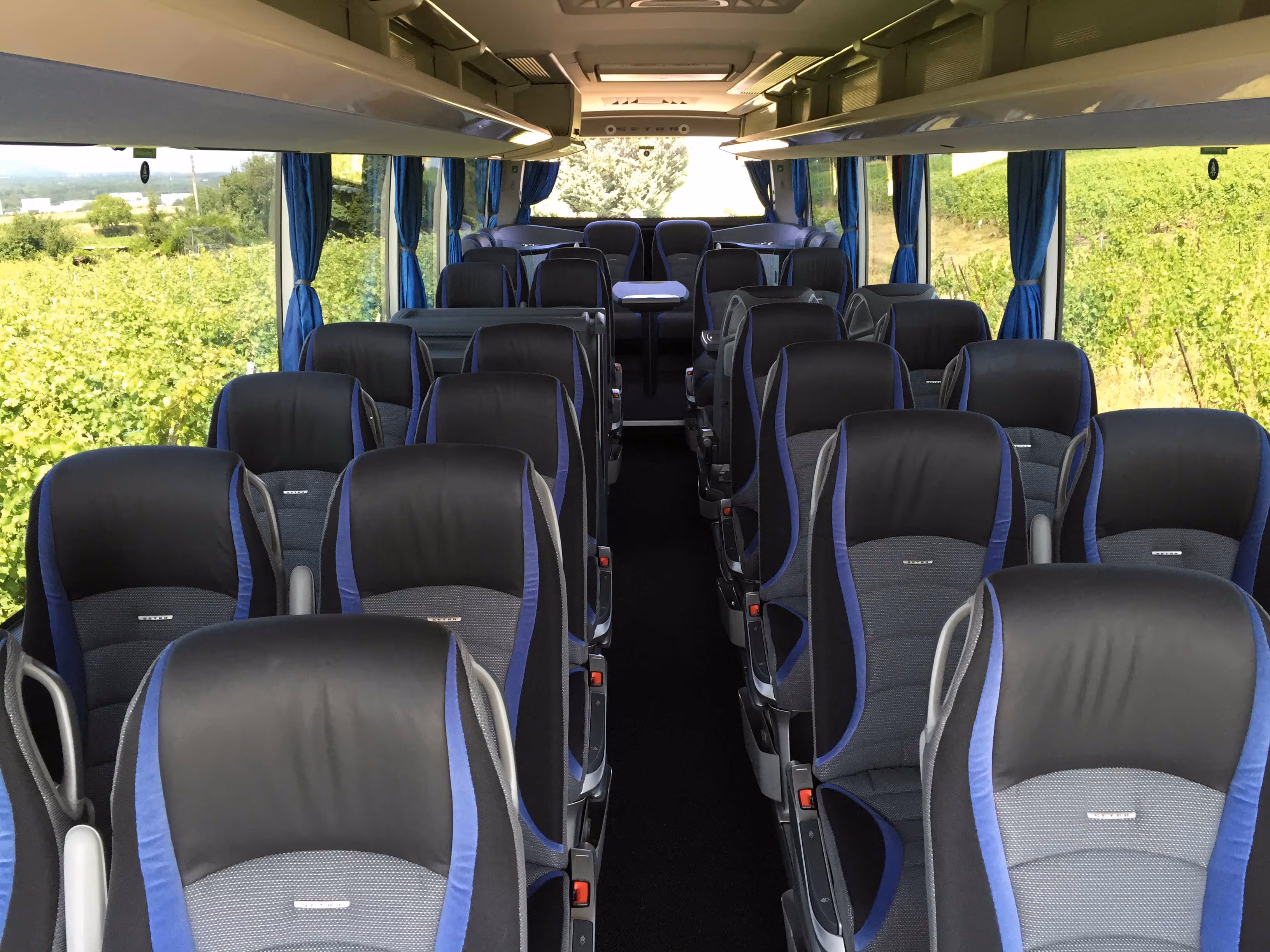 Vue de l'arrière vers l'avant de l'intérieur d'un autocar de luxe, montrant des rangées de sièges ergonomiques noirs et bleus et un couloir central moquetté.