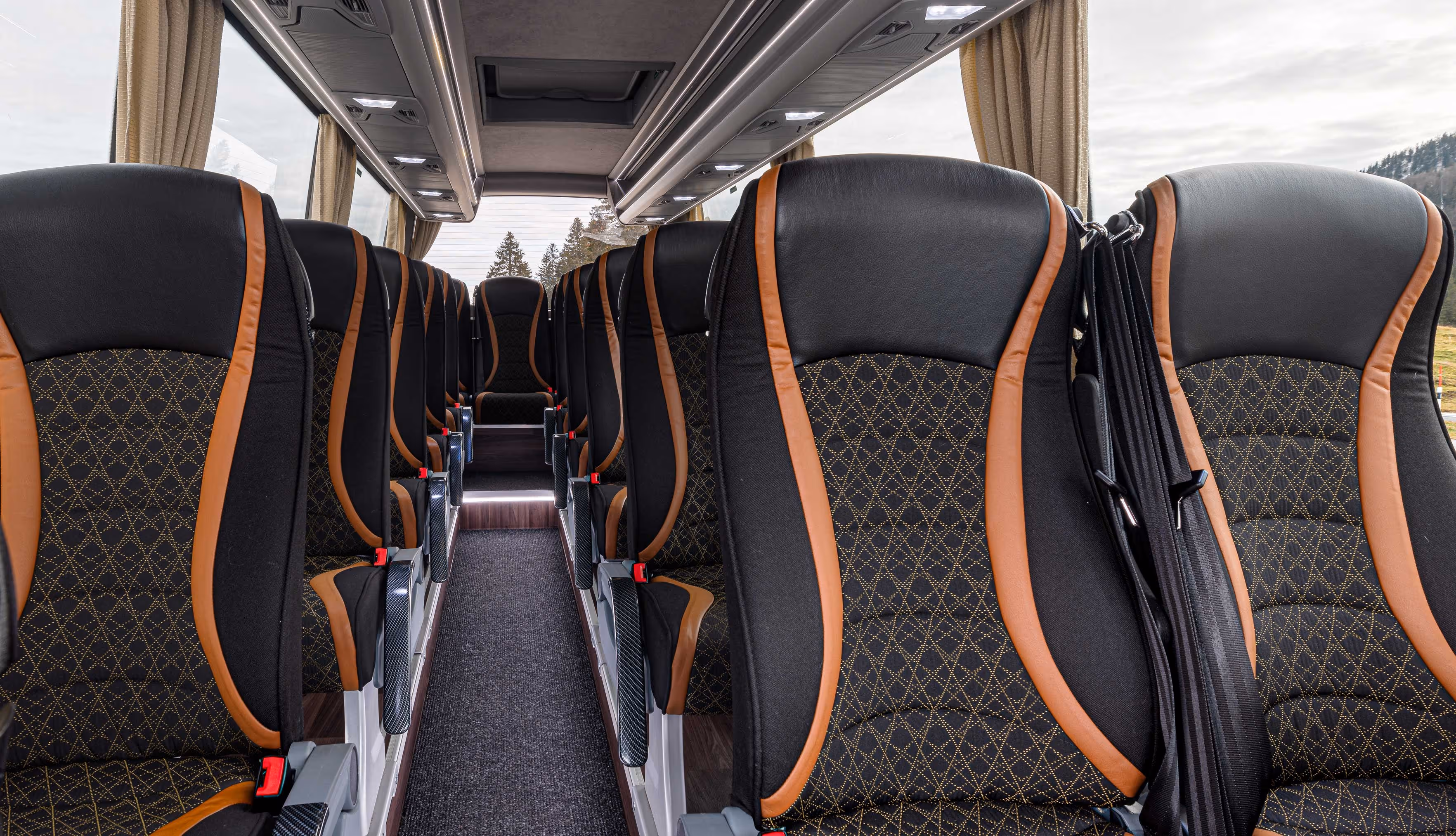 Intérieur luxueux d'un minibus montrant des rangées de sièges en cuir noir et orange avec des motifs de surpiqûres en losanges