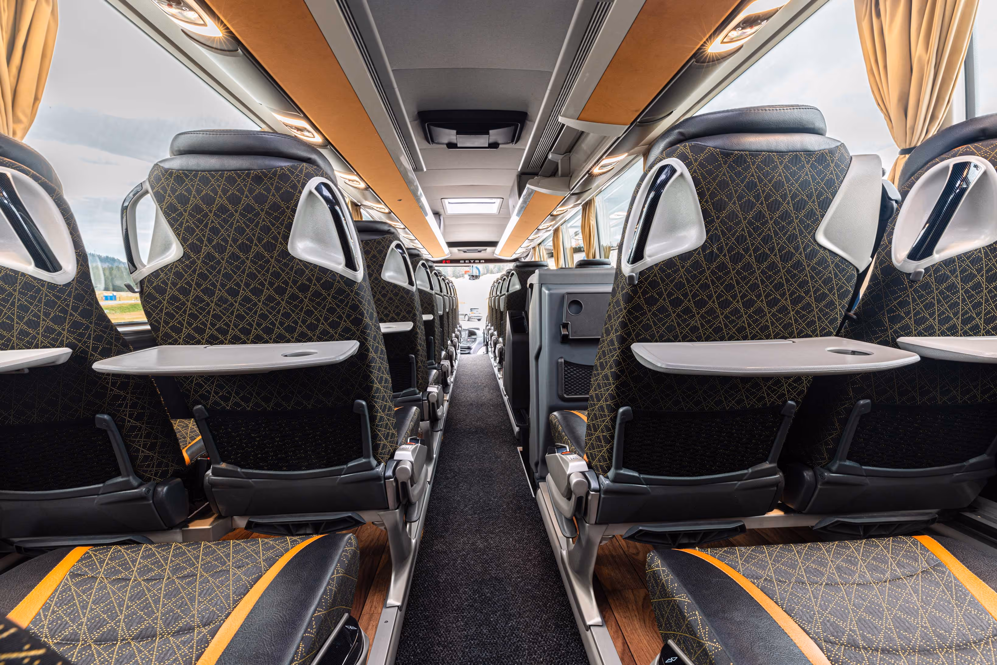 Vue de l'allée centrale d'un autocar haut de gamme avec des tablettes de dossier dépliées et un éclairage LED au plafond