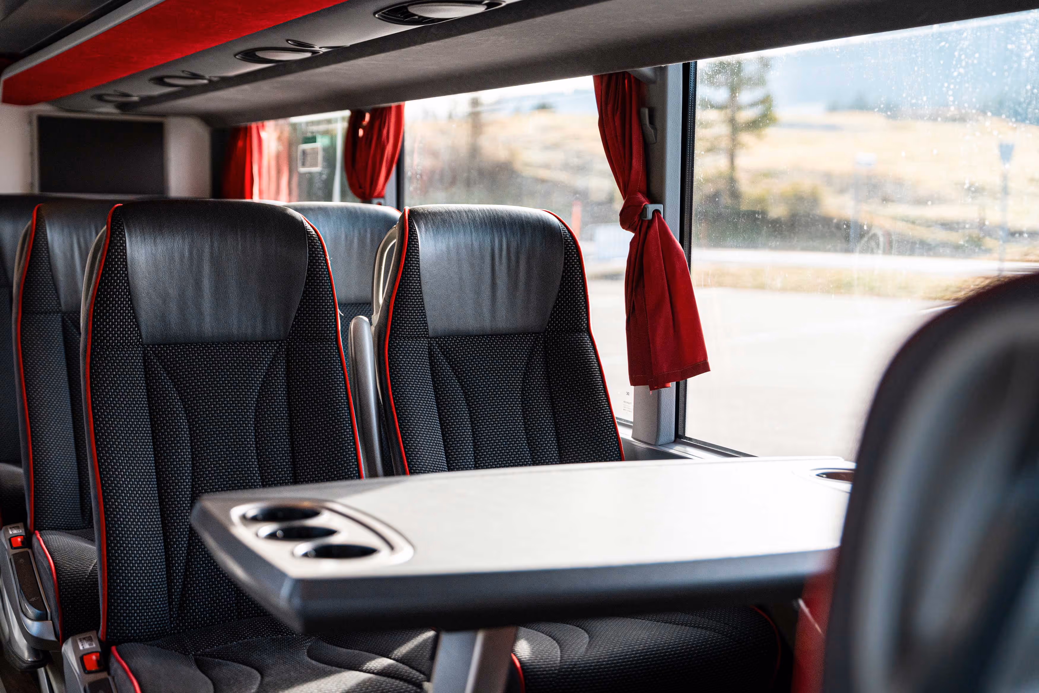 Zoom sur l'espace voyageur intérieur montrant des sièges noirs aux liserés rouges installés face à une table de voyage avec porte-gobelets, près d'une fenêtre avec rideaux rouges.