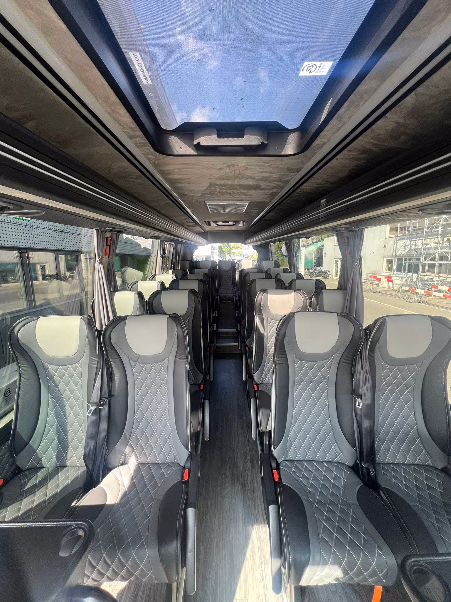 Vue de l'allée centrale d'un autocar moderne avec des sièges en cuir gris surpiqués de motifs en losanges et un toit panoramique vitré.