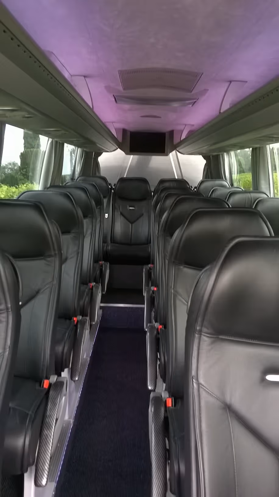 Vue de l'allée centrale d'un minibus avec des sièges en cuir noir et un éclairage de plafond aux tons violets.
