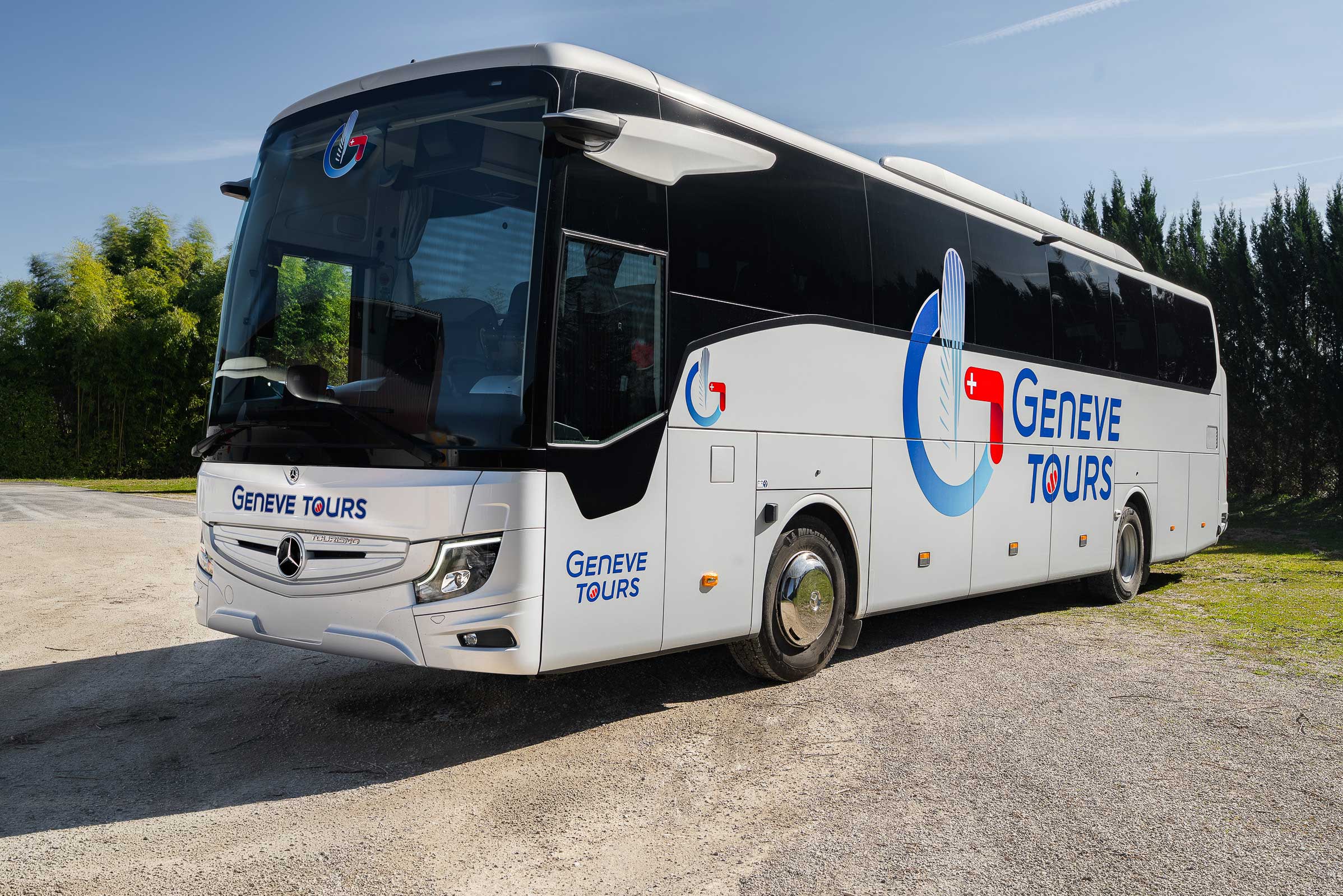 Vue extérieure d'un grand car Mercedes-Benz blanc et noir arborant fièrement le marquage Genève Tours sous un soleil éclatant.