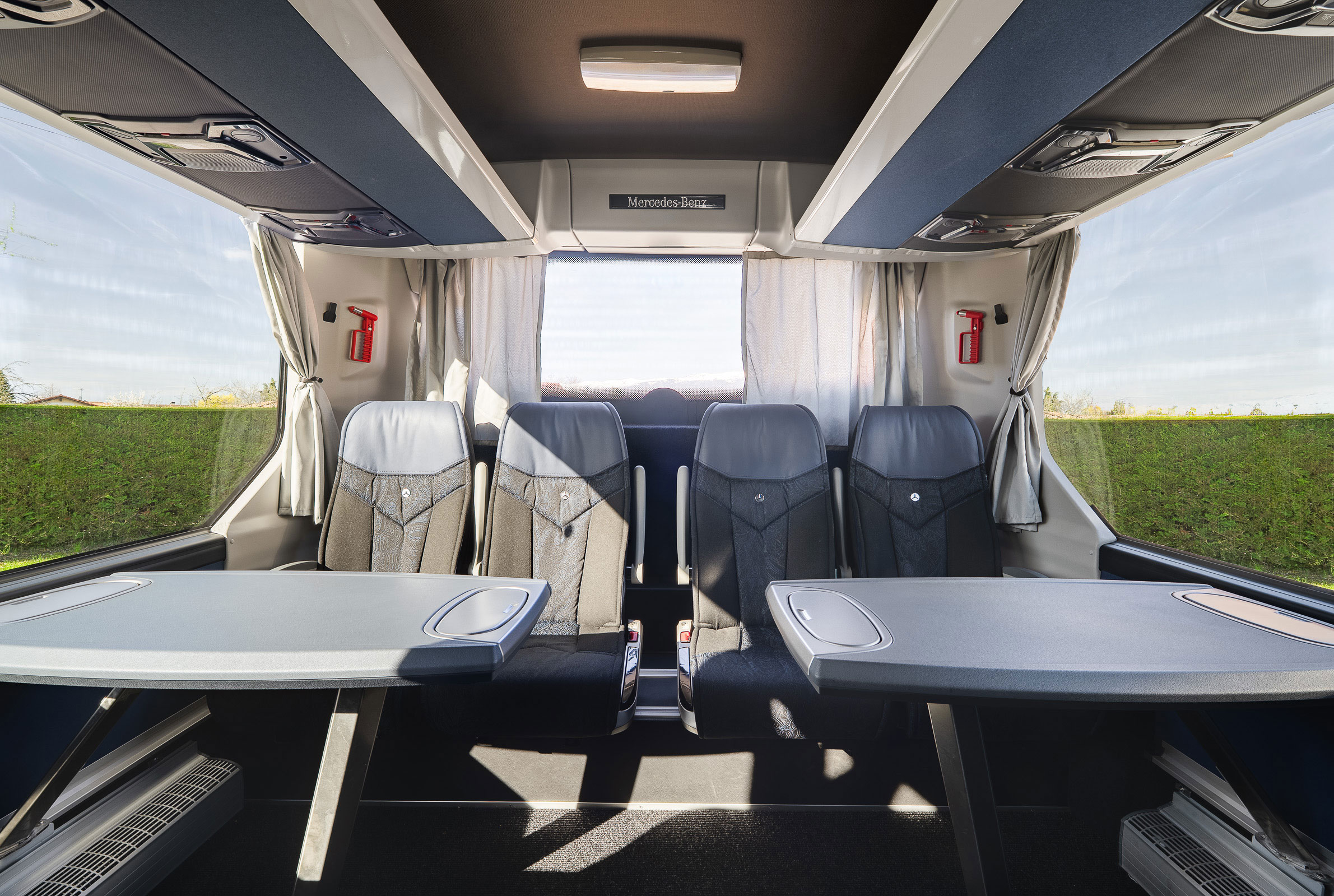 Aménagement intérieur d'un autocar avec deux grandes tables grises faisant face à une rangée de quatre sièges confortables au fond du véhicule.