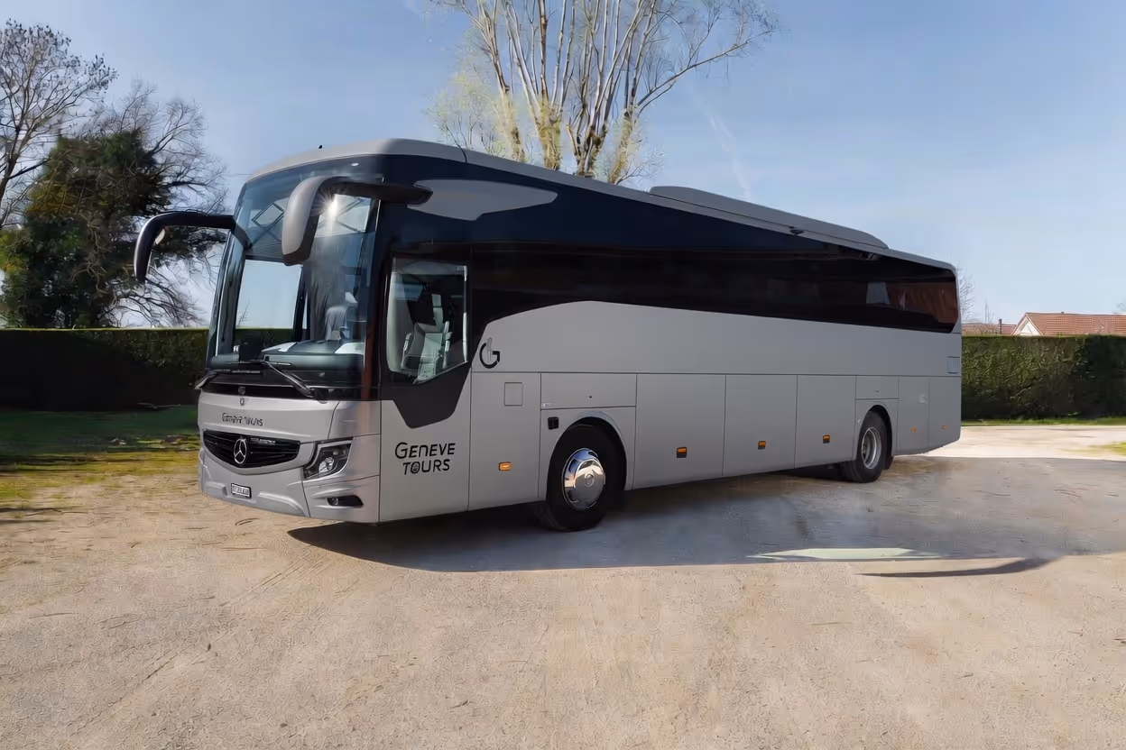 Vue extérieure de trois-quarts d'un autocar Mercedes-Benz blanc et noir, avec le logo "Genève Tours", stationné sur une esplanade ensoleillée.