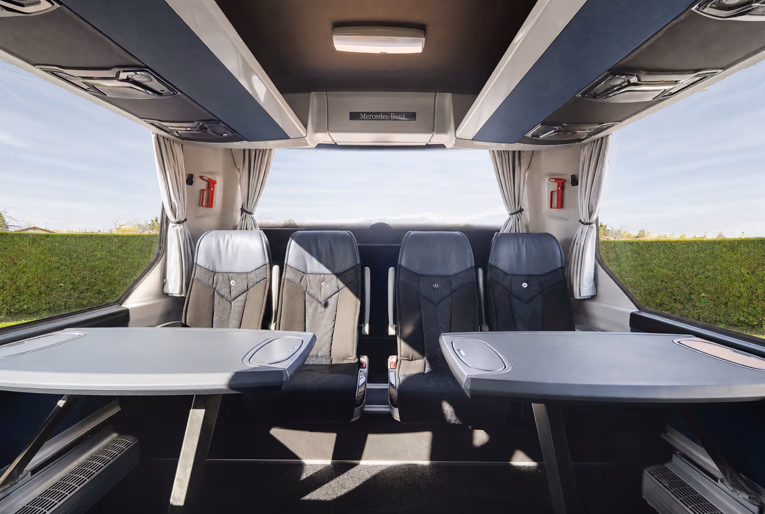 Aménagement intérieur d'un autocar avec deux grandes tables grises faisant face à une rangée de quatre sièges confortables au fond du véhicule.