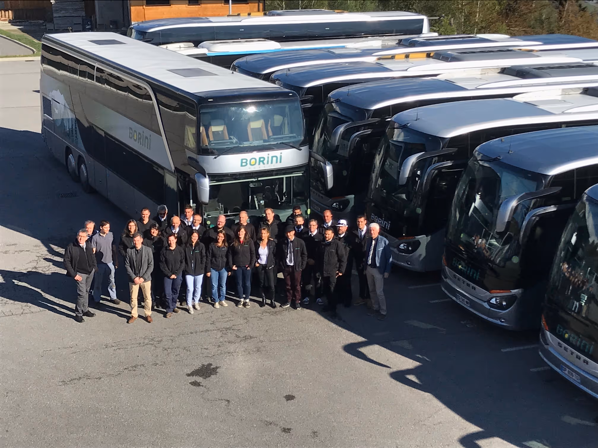 Groupe de personnes posant devant plusieurs autocars Borini garés dans une aire de stationnement.