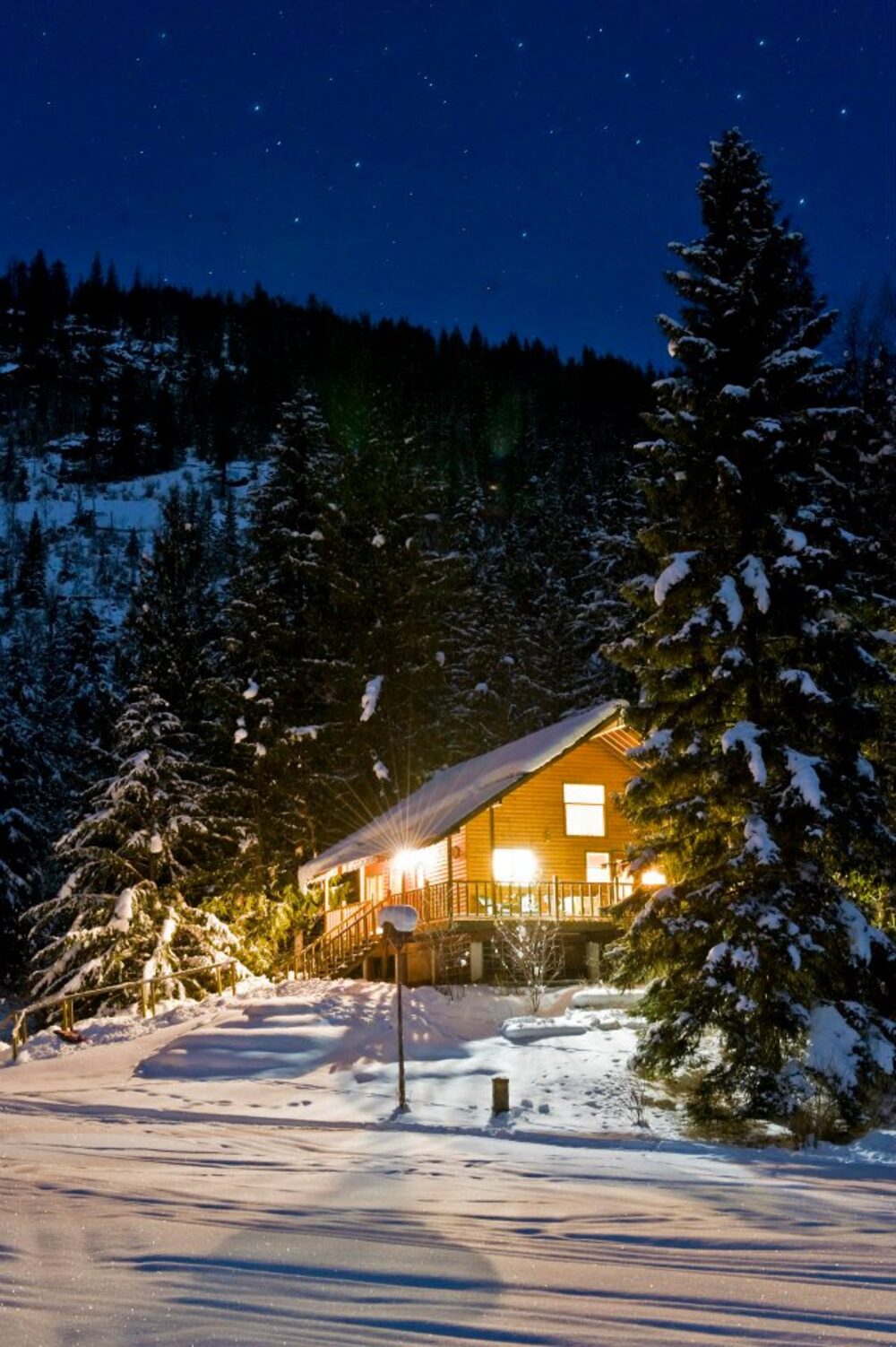 A warmly lit cabin under a clear starry winter sky, deep snow all around