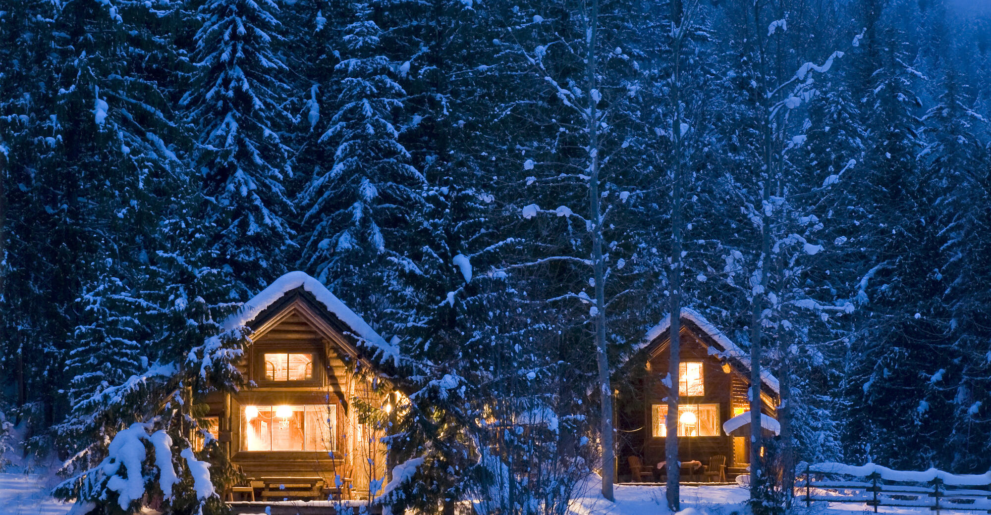 Cabins lit from within at dusk, surrounded by snow covered forest at The Healing Oasis in Lumby BC