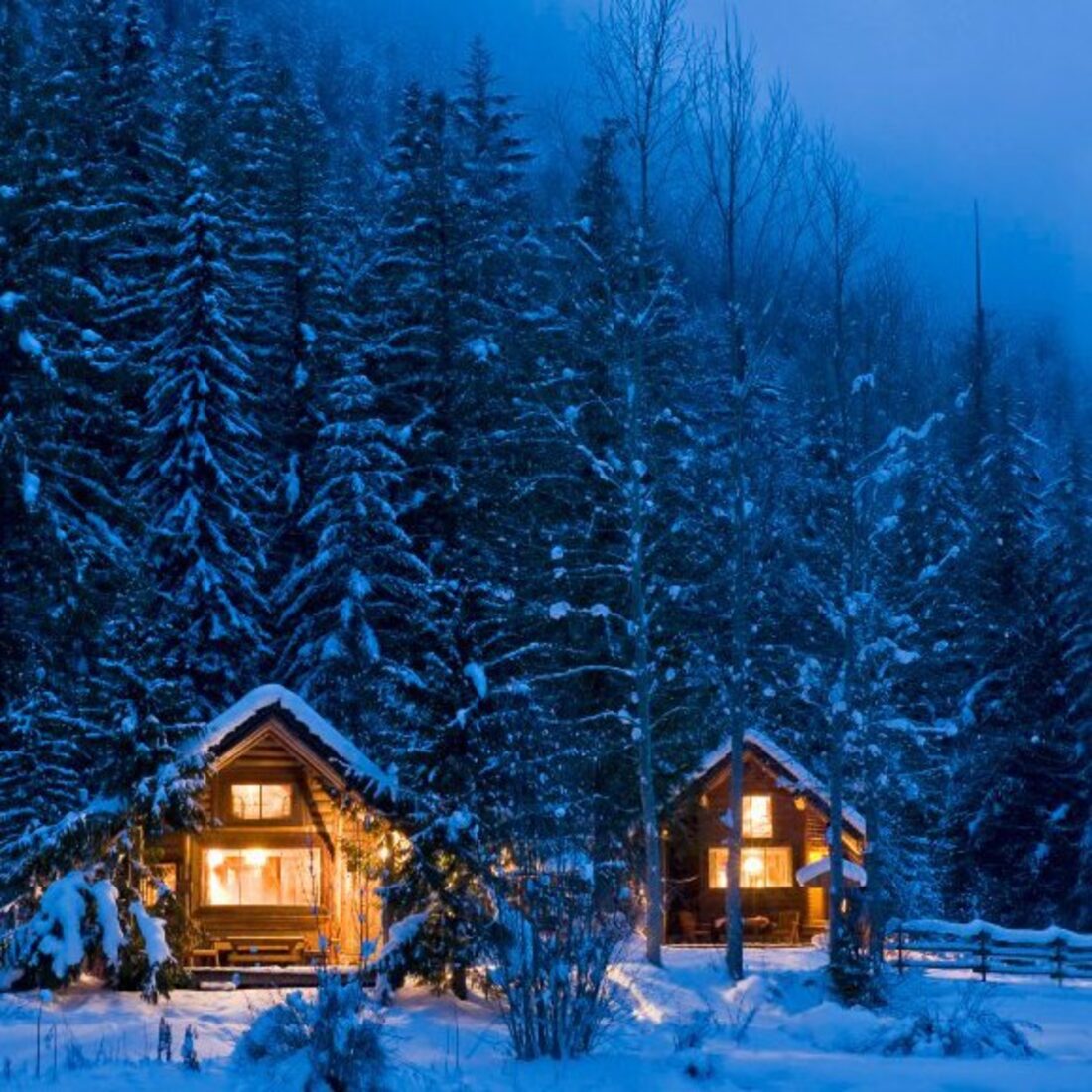 Warm light in the windows of snow covered cabins at blue hour