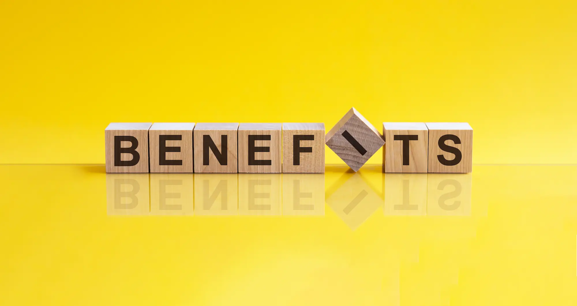 Lettered blocks in a straight row spelling out the word "benefits" in front of a yellow background. The "I" block is crooked.