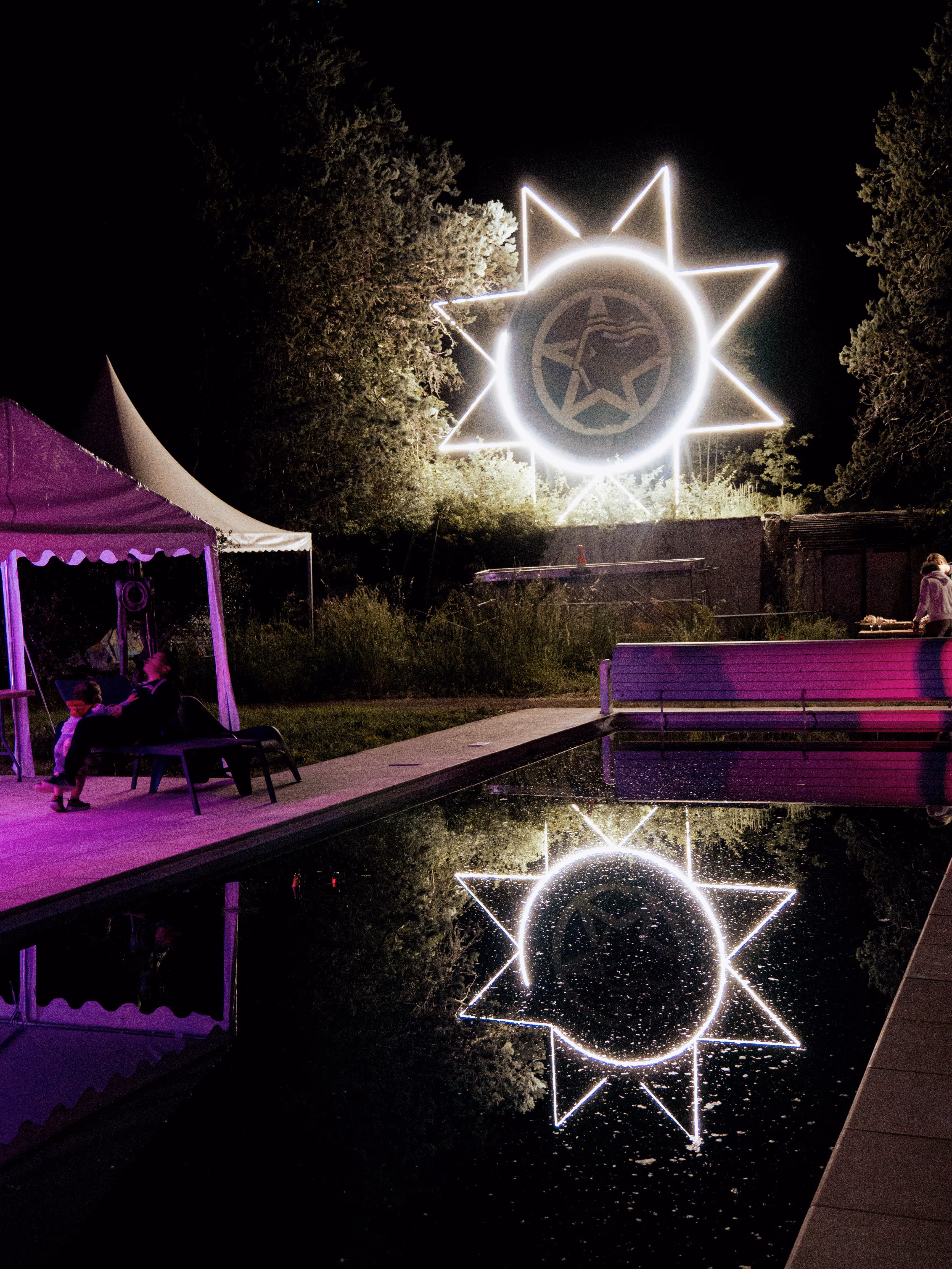 Installation lumineuse nocturne en forme d'étoile se reflétant dans un bassin, festival en plein air