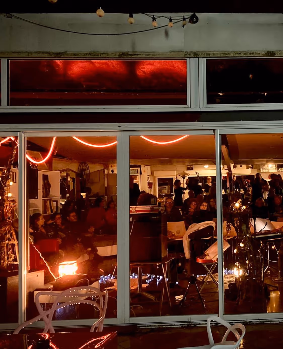 Vue extérieure nocturne d'un espace artistique avec des lumières rouges et des visiteurs visibles à travers les vitres