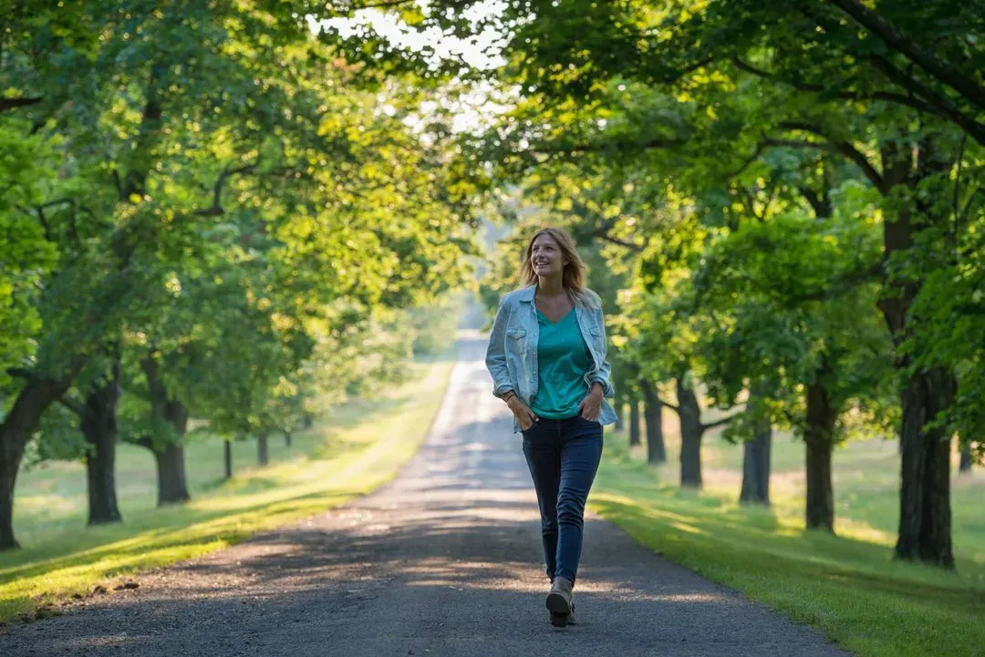 Vrouw die ontspannend wandelt op een boomrijke weg bij zonsondergang.