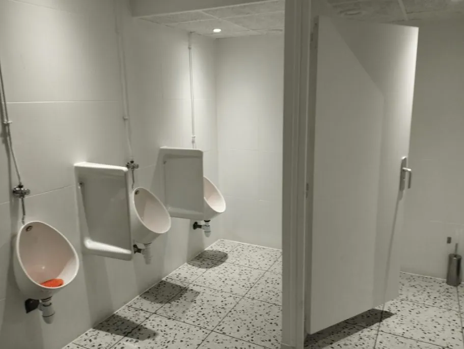 Sanitaires collectifs rénovés avec urinoirs muraux, carrelage blanc et cabine WC, aménagement de locaux professionnels