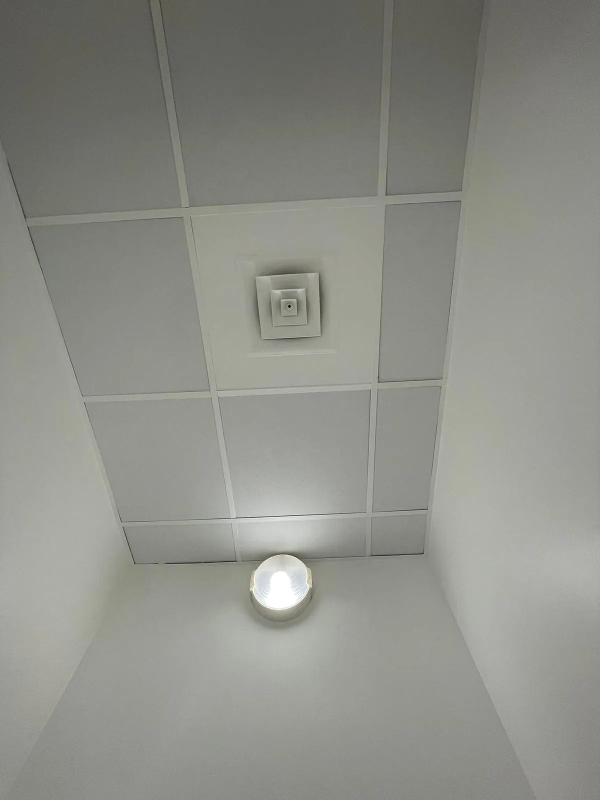 Diffuseur de climatisation carré encastré dans un faux plafond à dalles blanches avec plafonnier intégré