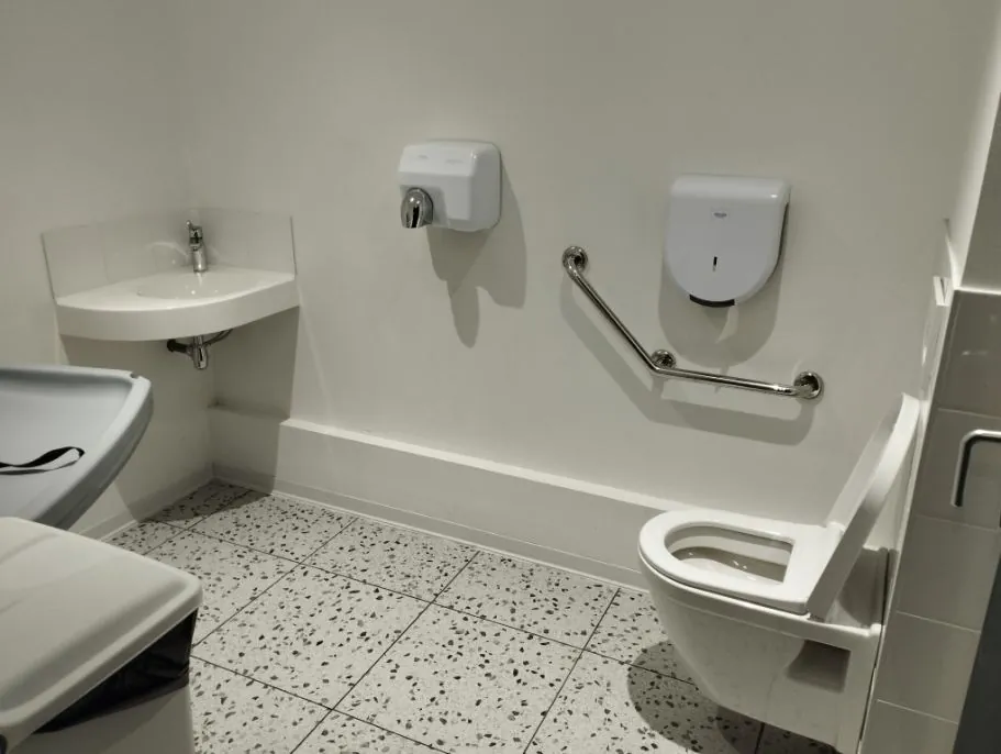 Sanitaire PMR accessible avec cuvette suspendue, barre d'appui chromée, lave-mains d'angle et sèche-mains automatique