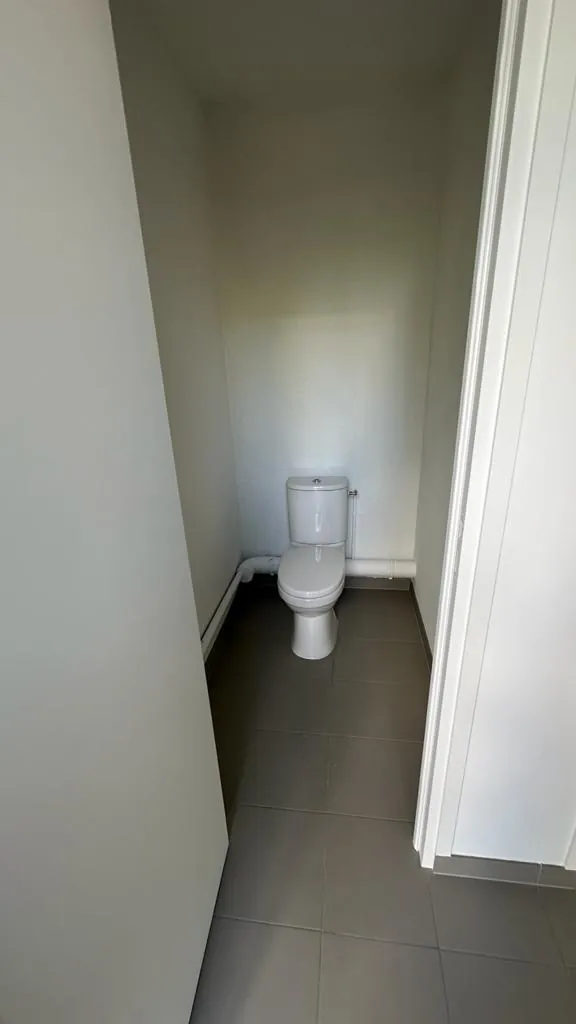 Cabine WC neuve avec cuvette à réservoir, carrelage marron au sol et canalisations apparentes, installation plomberie