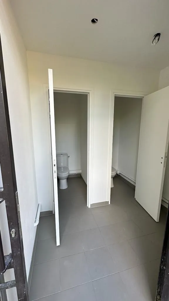 Couloir d'accès aux cabines WC neuves avec portes blanches et carrelage gris, installation sanitaire collective