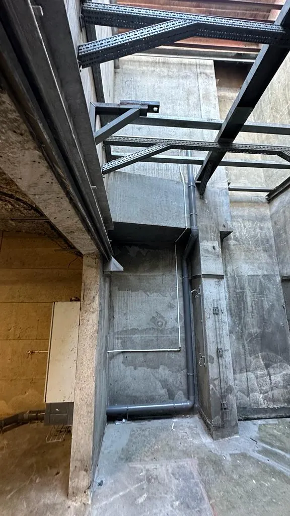 Gaine technique en béton brut avec charpente métallique, chemins de câbles et colonne de descente, chantier en régie