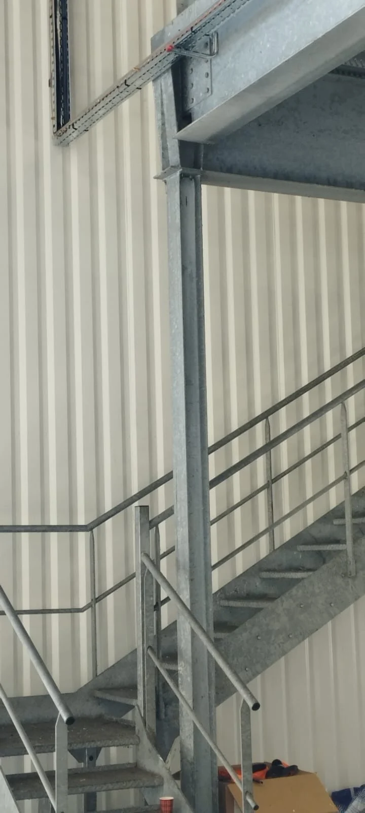 Escalier métallique industriel avec des rampes grises à l'intérieur d'un bâtiment aux murs en métal ondulé.