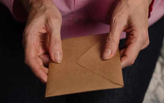 Mains tenant une enveloppe en papier kraft contre un fond sombre.