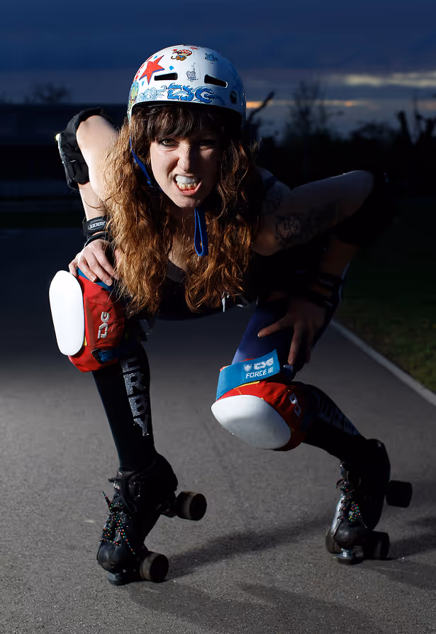 Homme portant un casque de sécurité blanc et un vêtement orange haute visibilité avec un patch ATEX, regardant vers la droite avec un bâtiment industriel en arrière-plan.