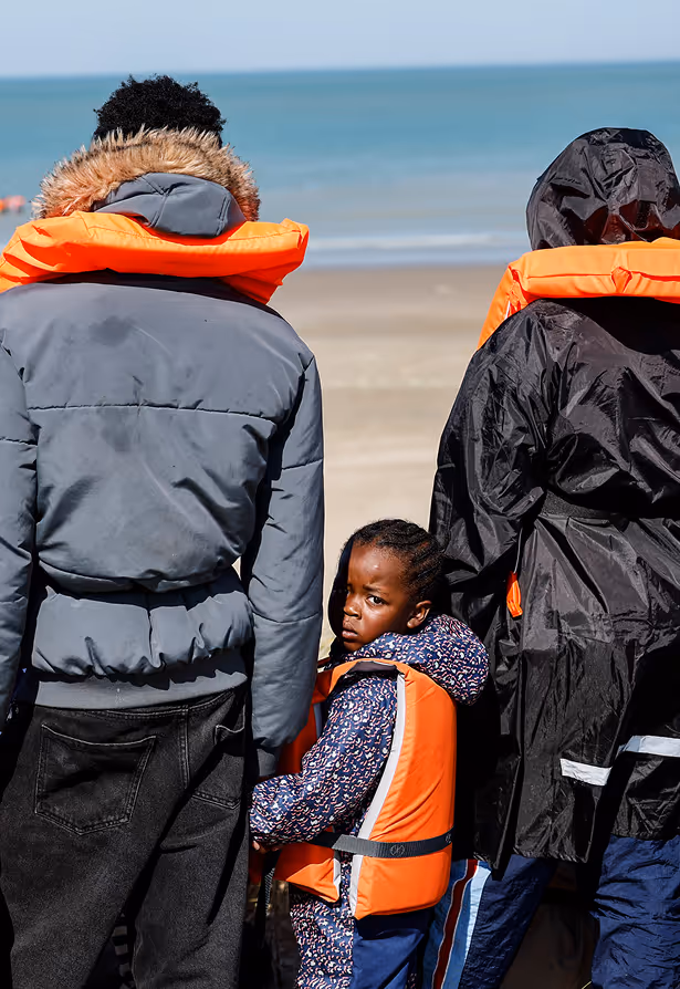 Homme portant un casque de sécurité blanc et un vêtement orange haute visibilité avec un patch ATEX, regardant vers la droite avec un bâtiment industriel en arrière-plan.