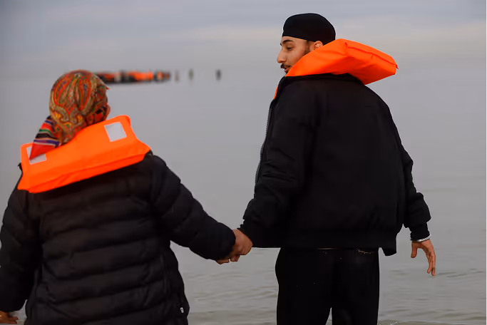 Une femme aux cheveux blonds coiffés en arrière portant une robe noire à col blanc regarde vers le haut avec un léger sourire.