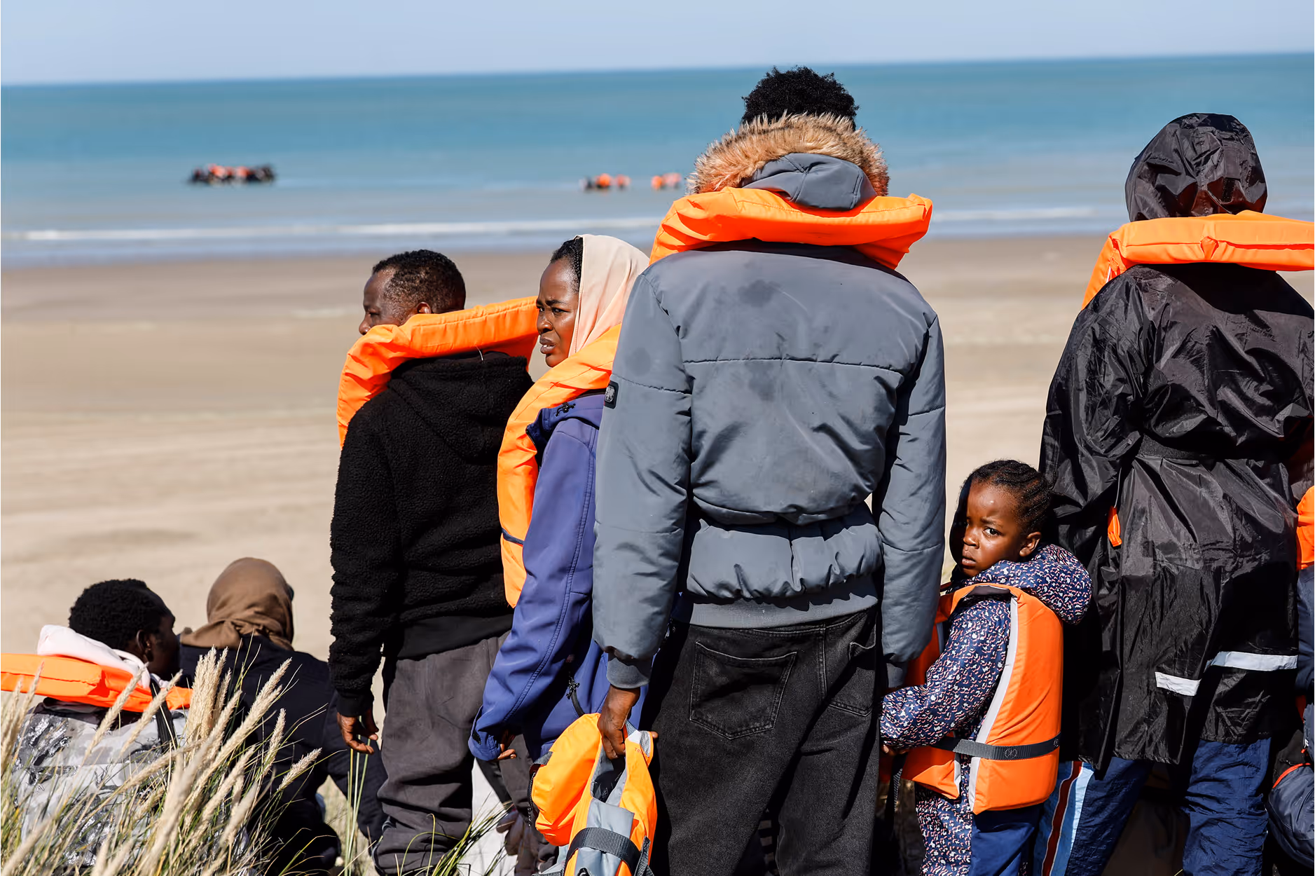 Homme portant un casque de sécurité blanc et un vêtement orange haute visibilité avec un patch ATEX, regardant vers la droite avec un bâtiment industriel en arrière-plan.
