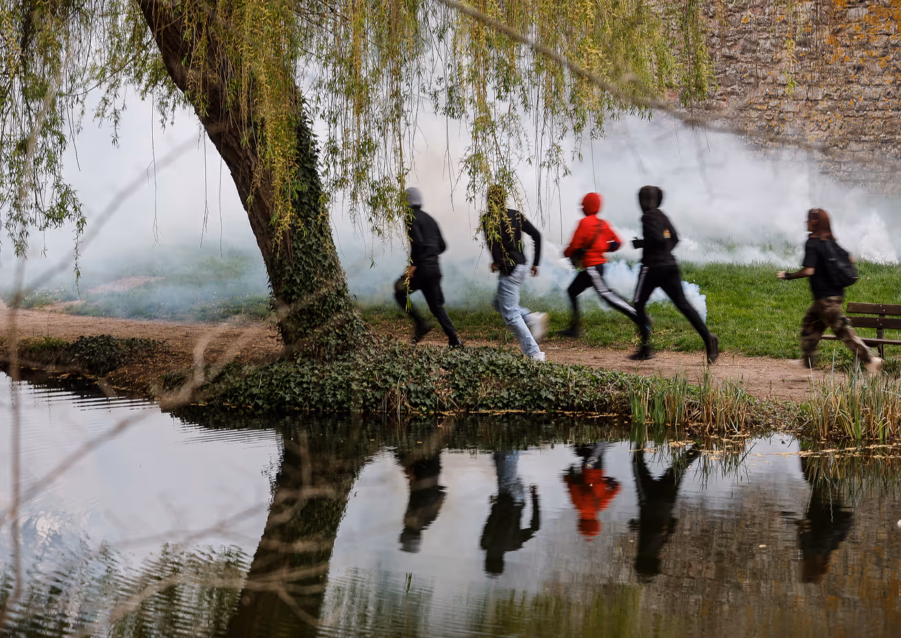 Groupe de cinq personnes courant sur un sentier près d'un arbre au bord d'un plan d'eau, avec de la fumée en arrière-plan.